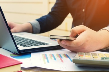 young business man using smartphone, laptop with data sheet, calculator on desk, analyzing and calculate, savings, finances, economy concept, sunlight effect, soft focus, selective focus, vintage tone