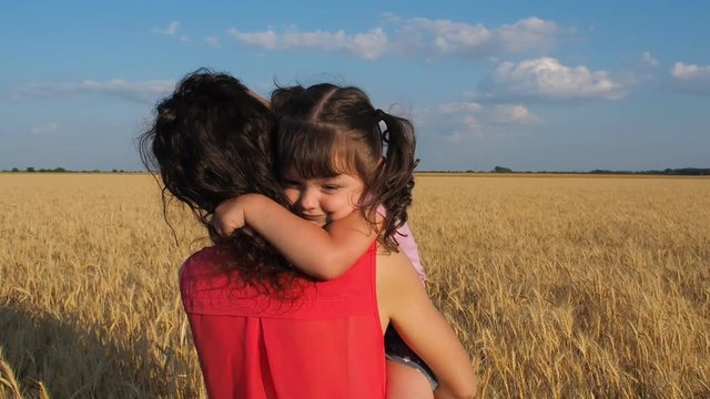 A child is hugging her mother. A little girl has a mother in her arms on a wheat field.