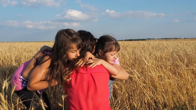 Children are hugging their mother on a wheat field. Happy daughters hug Mom.