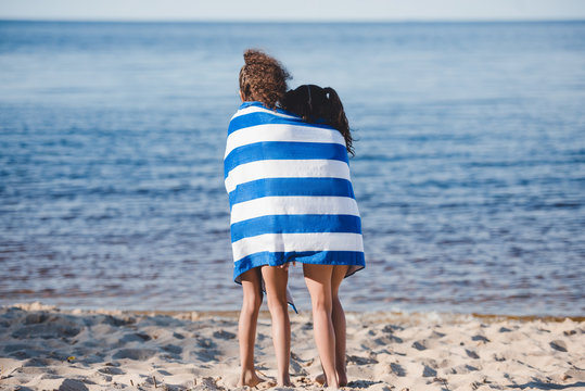 Back View Of Little Girls In Colorful Striped Towel Standing On Beach