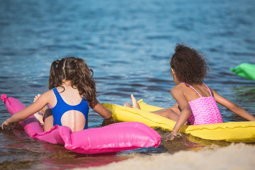 back view of little girls in swimsuits on inflatable mattresses at sea