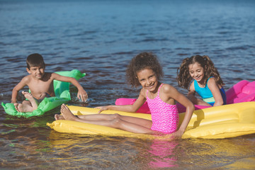 Obraz premium multiethnic little children swimming on colorful inflatable mattresses at sea together