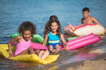 Obraz premium multiethnic little children swimming on colorful inflatable mattresses at sea together
