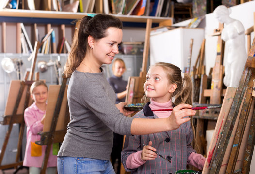 Female teacher helping girl during painting class