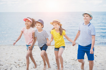 multicultural kids holding hands while walking on beach together