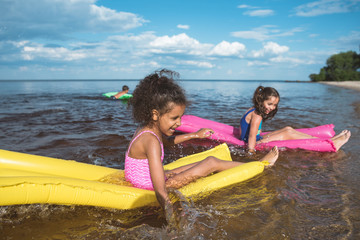 Obraz premium multicultural happy girls swimming together on inflatable mattresses at sea