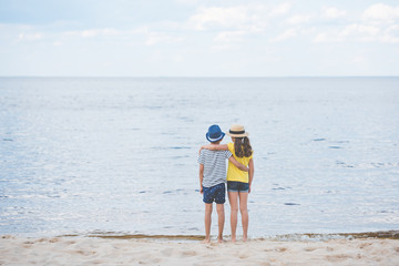 back view of girl and boy hugging each other while standing at seaside