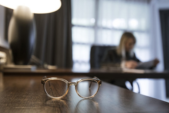 Spectacles on desk with businesswoman checking documents in the background