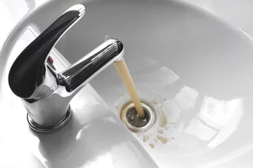 Abwaschbare Fototapete Wasser Wasserhahn mit fließendem schmutzigem schlammigem Wasser in einem Waschbecken