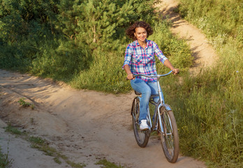 Naklejka premium Young woman rides a bicycle in the park on sunset background