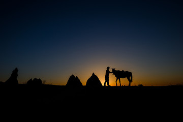 Fototapeta na wymiar Man and horse silhouette on the background of valley at Cappadocia,Anatolia,Turkey.The great tourist attraction of Cappadocia best places to fly with hot air balloons.Rocks looking like mushrooms.