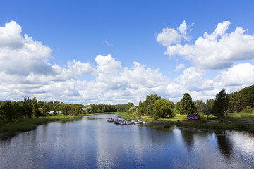 Beautiful scenery in the countryside next to a river in Finland. Sunny summer day with some clouds in the sky. Traditional village view.