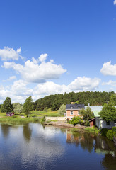 Fototapeta na wymiar Beautiful scenery in the countryside next to a river in Finland. Sunny summer day with some clouds in the sky. Traditional village view.