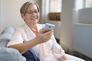 lächelnde seniorin schaut auf ihr mobiltelefon