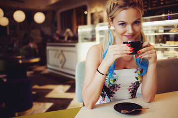 Trendy girl with bright colored hair, sitting in cafe, drink coffee and eat dessert