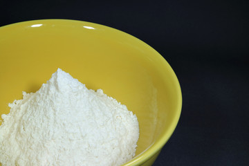 Pure white raw flour in yellow ceramic bowl, isolated on black background with free space for text and design 