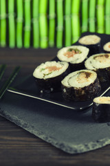 Sushi rolls on black plate and wooden background
