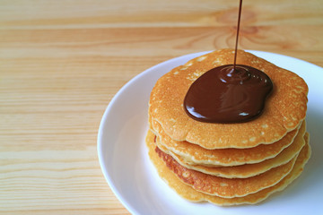 Melted Belgian Chocolate Being Poured on Stack of Pancakes, with Free Space on Wooden Table for Text or Design 