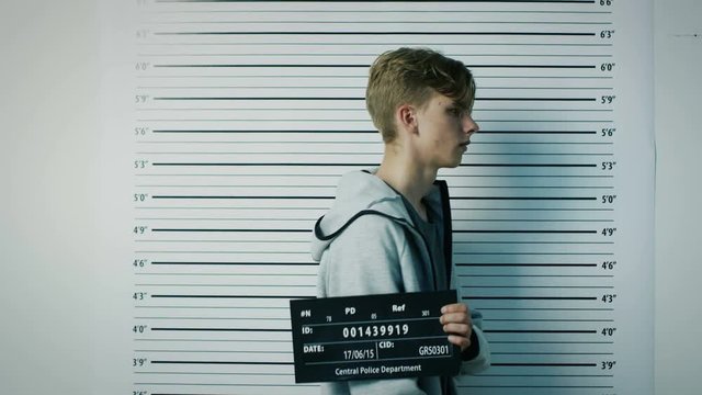 In a Police Station Arrested Teenage Delinquent Poses for Side, Front View Mugshot. He is Heavily Bruised. Height Chart in the Background. Shot on RED EPIC-W 8K Helium Cinema Camera.