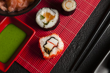 Sushi rolls, ginger and wasabi on red mat and black table