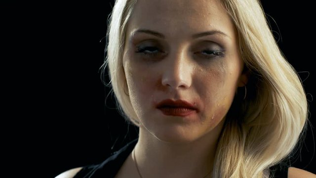 Close-up Shot Sad Crying Bruised Blonde Woman Looking Down and Then Into the Camera. Violence Theme. Shot on Isolated Black Background. Shot on RED EPIC-W 8K Helium Cinema Camera.