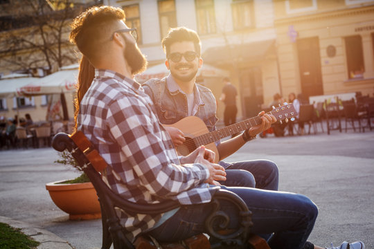 Group of people hangout at the city street.They sitting on bench ,singing and playing guitar.