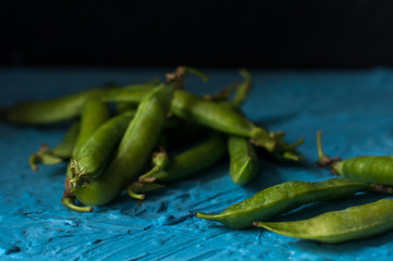 Young organic green pea pods and peas over blue texture background. Close up. Harvest, healthy eating.