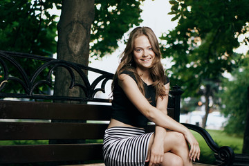 Young beautiful woman sits on a summer bench in a park in the city