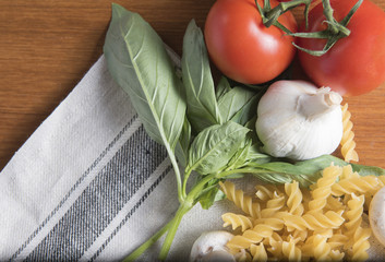 Dried fusilli pasta with tomatoes, basil and garlic on a wooden background 