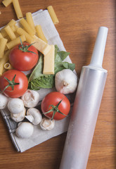 Vertical image of dried rigatoni pasta with tomatoes, garlic, basil and cheese on a wooden background