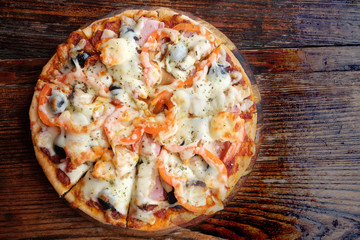 Homemade pizza with melting cheese tomatoes olive and ham. Top view on dark wooden table.