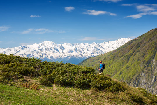 Man traveler is standing on a green mountain slope