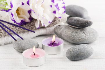 Fototapeta na wymiar Spa composition with towels, lit candles, purple aroma sticks