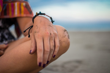 Girl sitting on the beach focus on the hand and the knee. Hand with cool bracelet and purple nails chilling on the sand