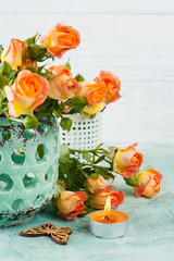 Fresh orange roses flowers in mint vase and lit candle