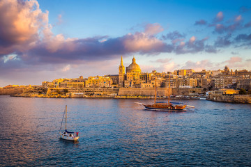 Fototapeta na wymiar Valletta, Malta - Sail boats at the walls of Valletta with Saint Paul's Cathedral and beautiful sky and clouds in the morning