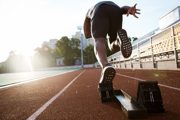 Back view of a young male athlete launching off the start line - obrazy, fototapety, plakaty