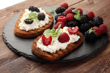 Bread with cheese cream and blackberries and raspberries for lunch table. Sharing antipasti on party or summer picnic time over wooden rustic background.