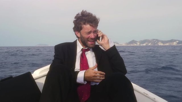Man in suit with a briefcase talking on his smartphone on a boat in the middle of the ocean