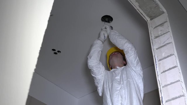 electrician man with helmet cut holes in plasterboard ceiling for light install