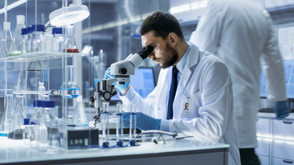Research Scientist Looks into Microscope in Research Centre. He's Conducts Experiments in Modern...