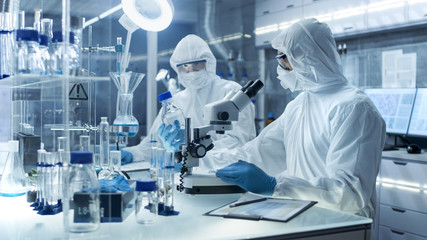 In a Secure High Level Laboratory Scientists in a Coverall Conducting a Research. Chemist Adjusts Samples in a  Petri Dish with Pincers. - obrazy, fototapety, plakaty