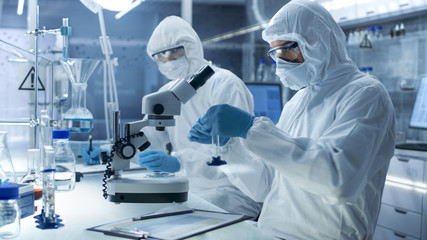 In a Secure High Level Laboratory Scientists in a Coverall Conducting a Research. Chemist Adjusts...
