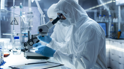 In a Secure High Level Laboratory Scientists in a Coverall Conducting a Research. Chemist Adjusts Samples in a  Petri Dish with Pincers.