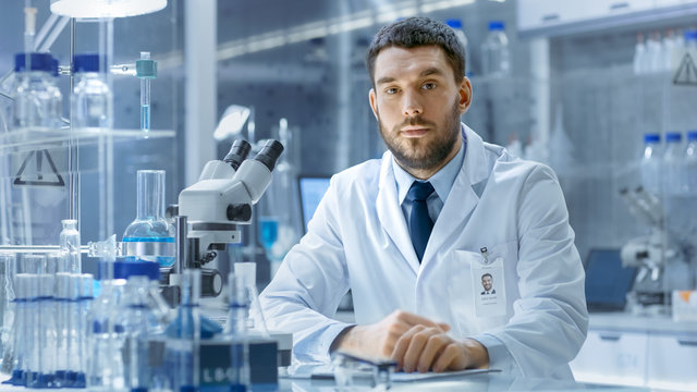 In a Secure High Level Laboratory Scientists in a Coverall Conducting a Research. Chemist Adjusts Samples in a  Petri Dish with Pincers.