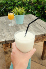 Closeup of female hand holding glass of coconut smoothie with straw while sitting at cafe outdoors. POV
