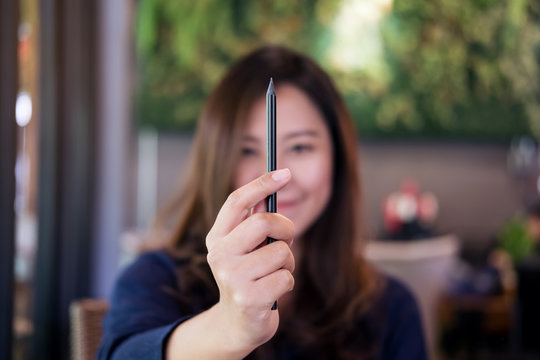 A beautiful Asian woman holding and raising black pencil to measurement in drawing process in cafe with green vertical garden background