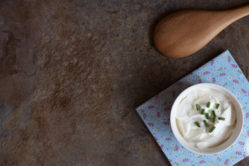 Sour cream in a bowl on brown marble background. Top view with copy space