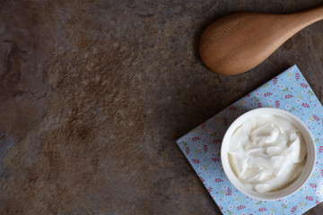 Sour cream in a bowl on brown marble background.