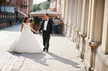 Amazing young attractive newly married couple walking and posing in the downtown with beautiful and ancient architecture on the background on their wedding day.